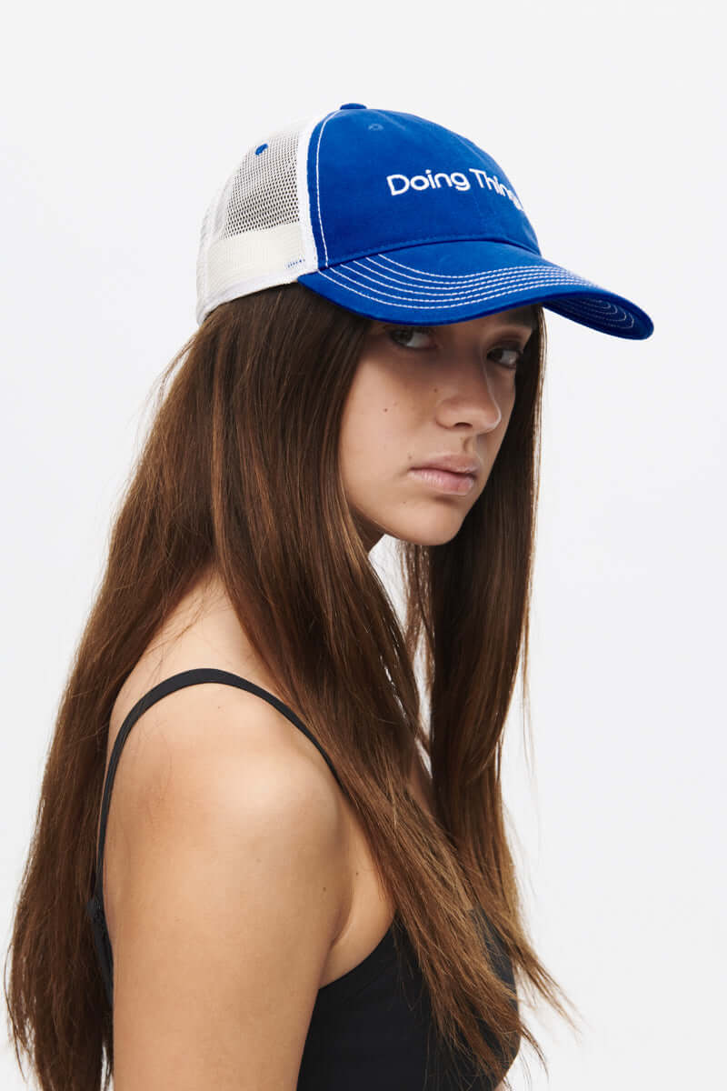 Profile view of a woman wearing a Doing Things Trucker Hat in blue, showcasing style and comfort.