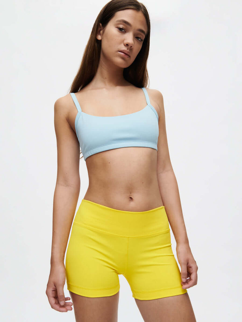 Model wearing the Gemini 3" Short in vibrant yellow, paired with a light blue crop top. Perfect for active lifestyles!