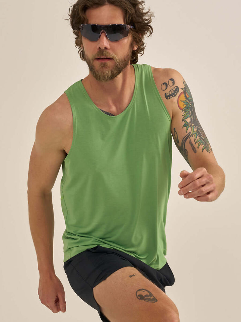 Man wearing ThinkFast Vent Tank CL and sunglasses, running with style in a vibrant green tank.
