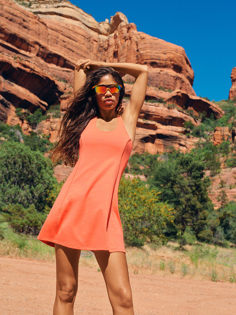 A model wearing the Doing Things Dress in a vibrant orange color, showcasing sporty style amidst scenic red rock formations.