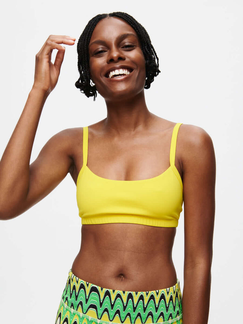 Model wearing the Solar Bra in bright yellow, featuring adjustable straps and a soft elastic band.