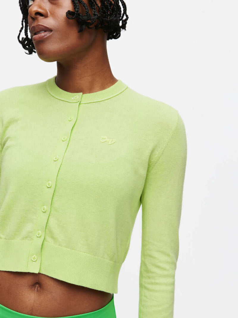 Model wearing a vibrant green Sugar Cardigan made of soft cotton cashmere, featuring hand-embroidered OV signature.