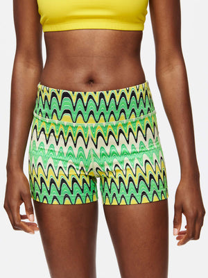 Model wearing vibrant TechSweat 3" Short with a pattern of green waves and a yellow top, perfect for workouts.