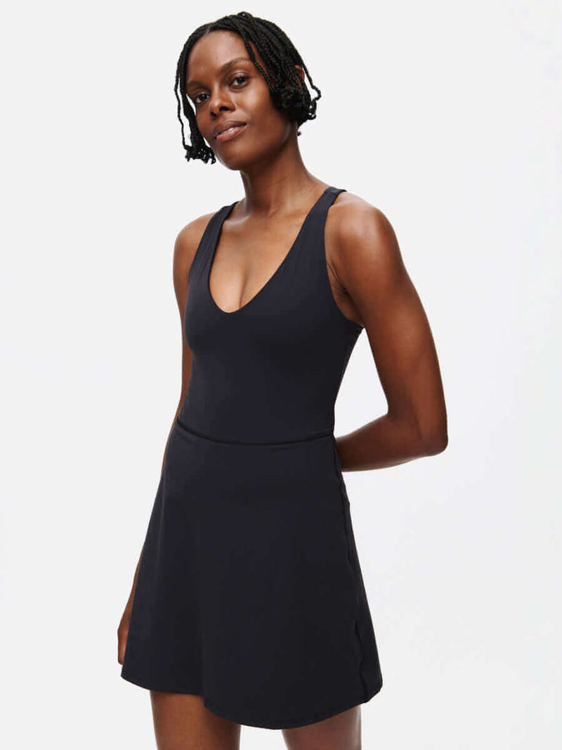 Woman in a black Volley Dress featuring a V-neck and fit-and-flare silhouette with built-in shorts.